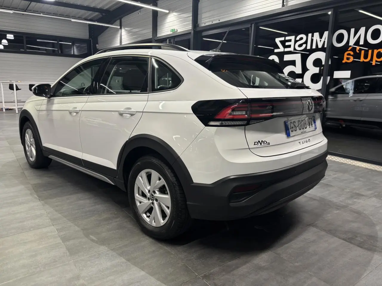 Vue 3/4 arrière droite du Volkswagen Taigo blanc avec jantes alliage et feux arrière LED dans un showroom.