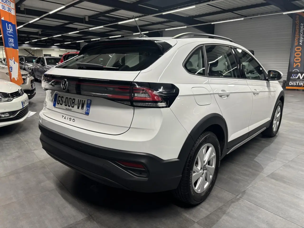 Vue 3/4 arrière droite d'un Volkswagen Taigo blanc avec feux arrière noirs et jantes alliage en showroom.