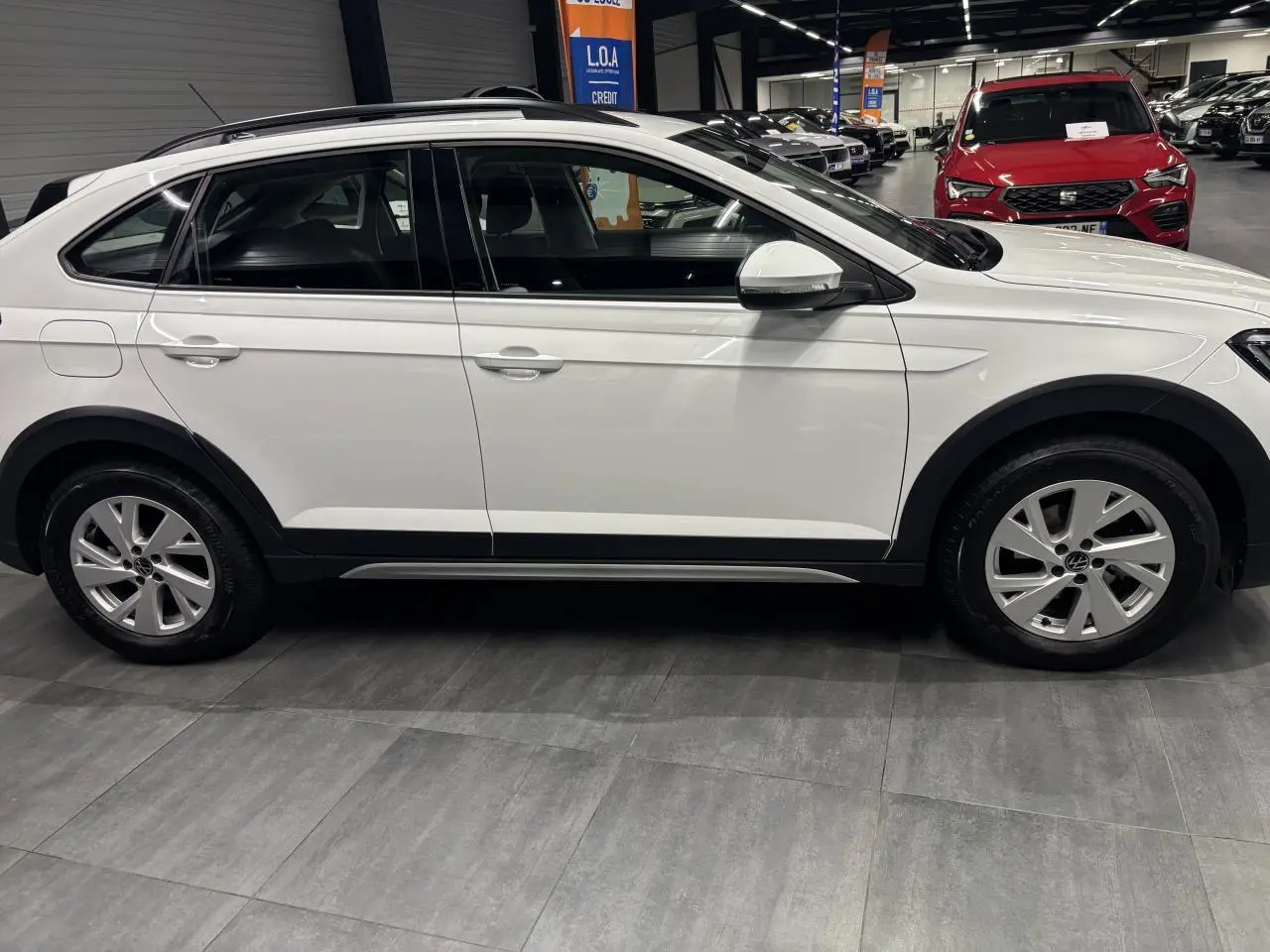 Vue de profil côté gauche d'un Volkswagen Taigo blanc 2023 avec jantes alliage et protections noires sur les passages de roues.