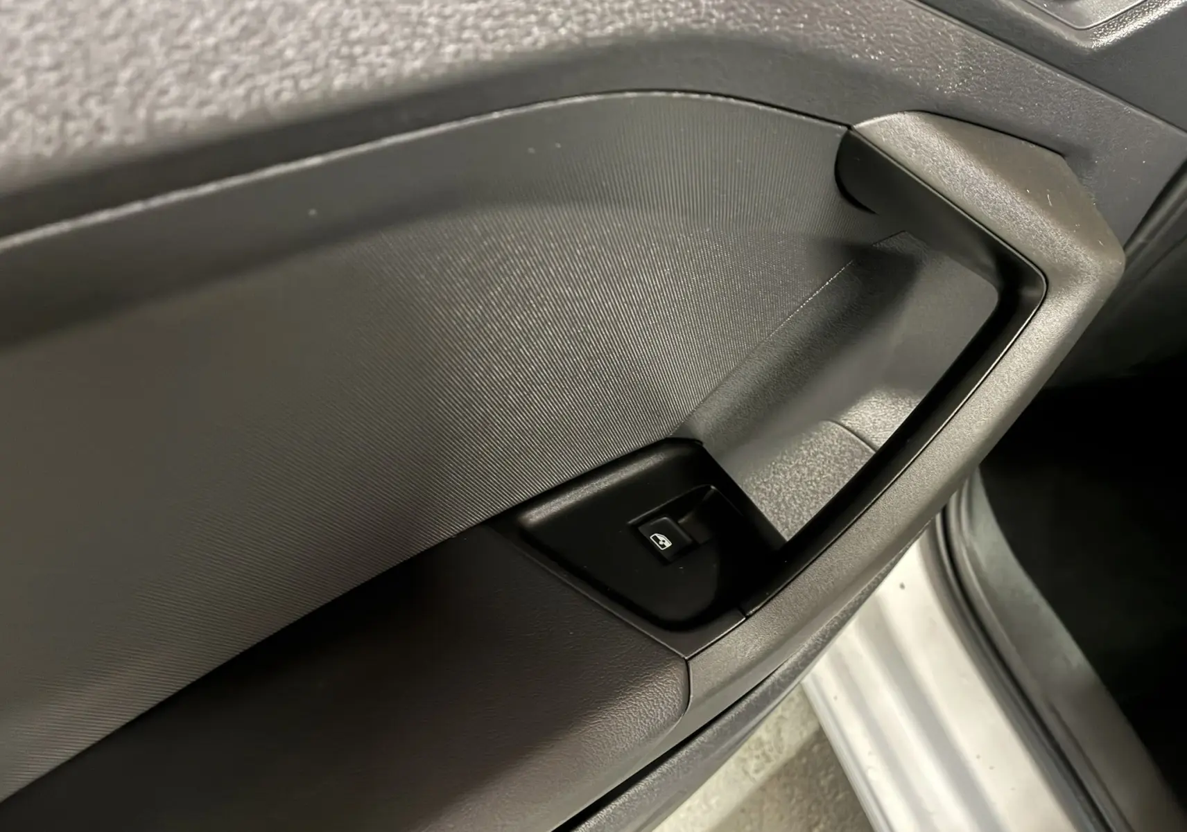 Gros plan sur la commande de lève-vitre côté gauche d’une Audi A1 blanche, intérieur noir texturé.