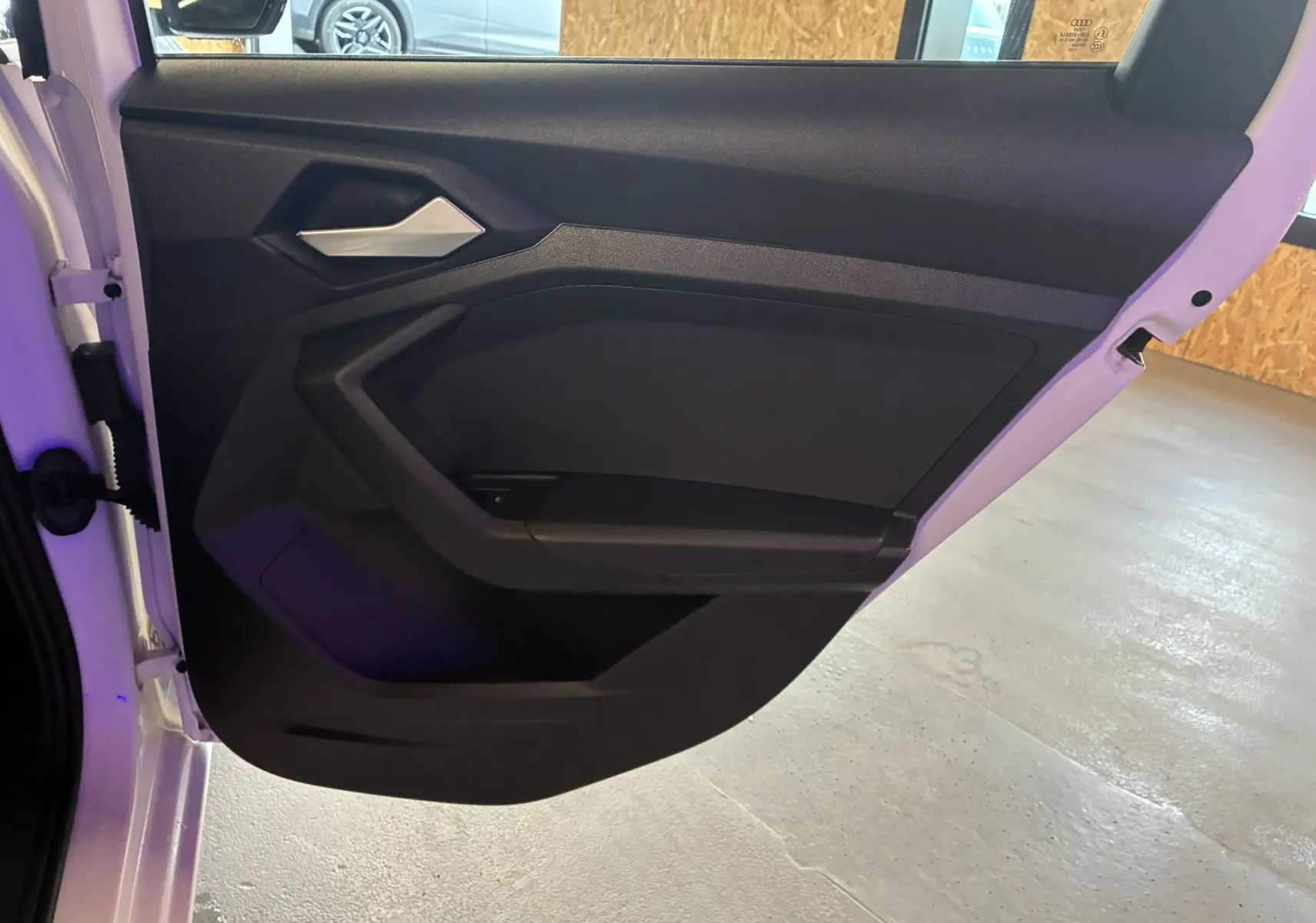 Vue intérieure de la porte arrière gauche noire d'une Audi A1 blanche 2022, avec poignée argentée et panneau épuré.