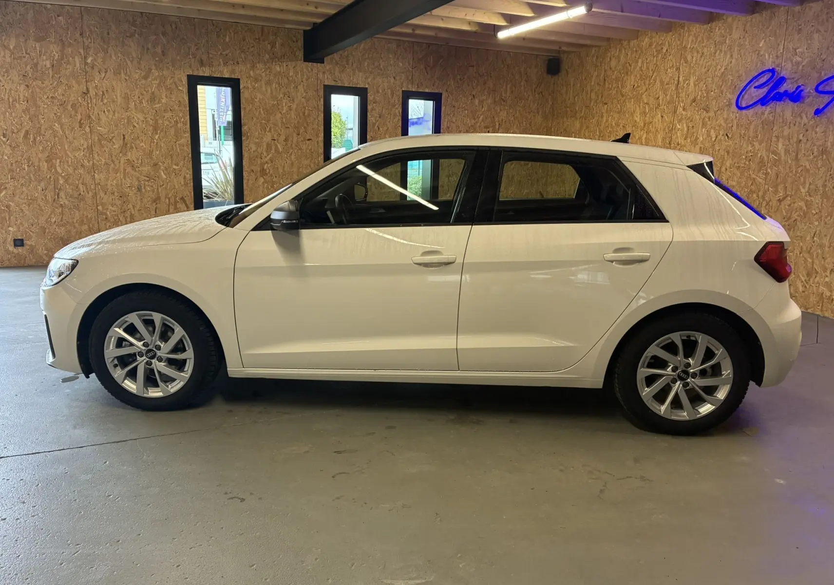 Audi A1 blanche vue de profil côté gauche, avec jantes alu 17 pouces dans un garage intérieur.