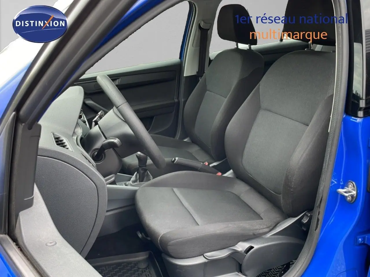 Vue intérieure côté conducteur de la Skoda Fabia 1.0 TSI bleu énergie avec sièges tissu noirs et volant visible.