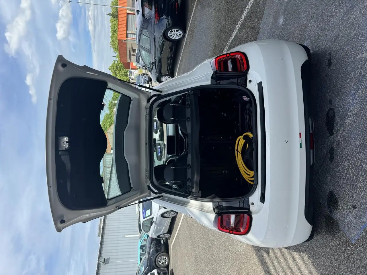 Vue arrière d'une Fiat 500 électrique blanche 2022 avec coffre ouvert et câble de recharge visible dans un parking.