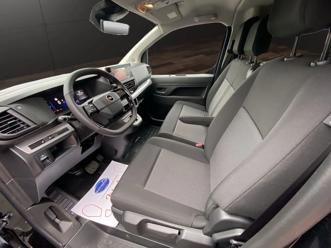 Intérieur avant de l'Opel Vivaro noir 2025, vue côté conducteur montrant sièges tissu gris et tableau de bord moderne.