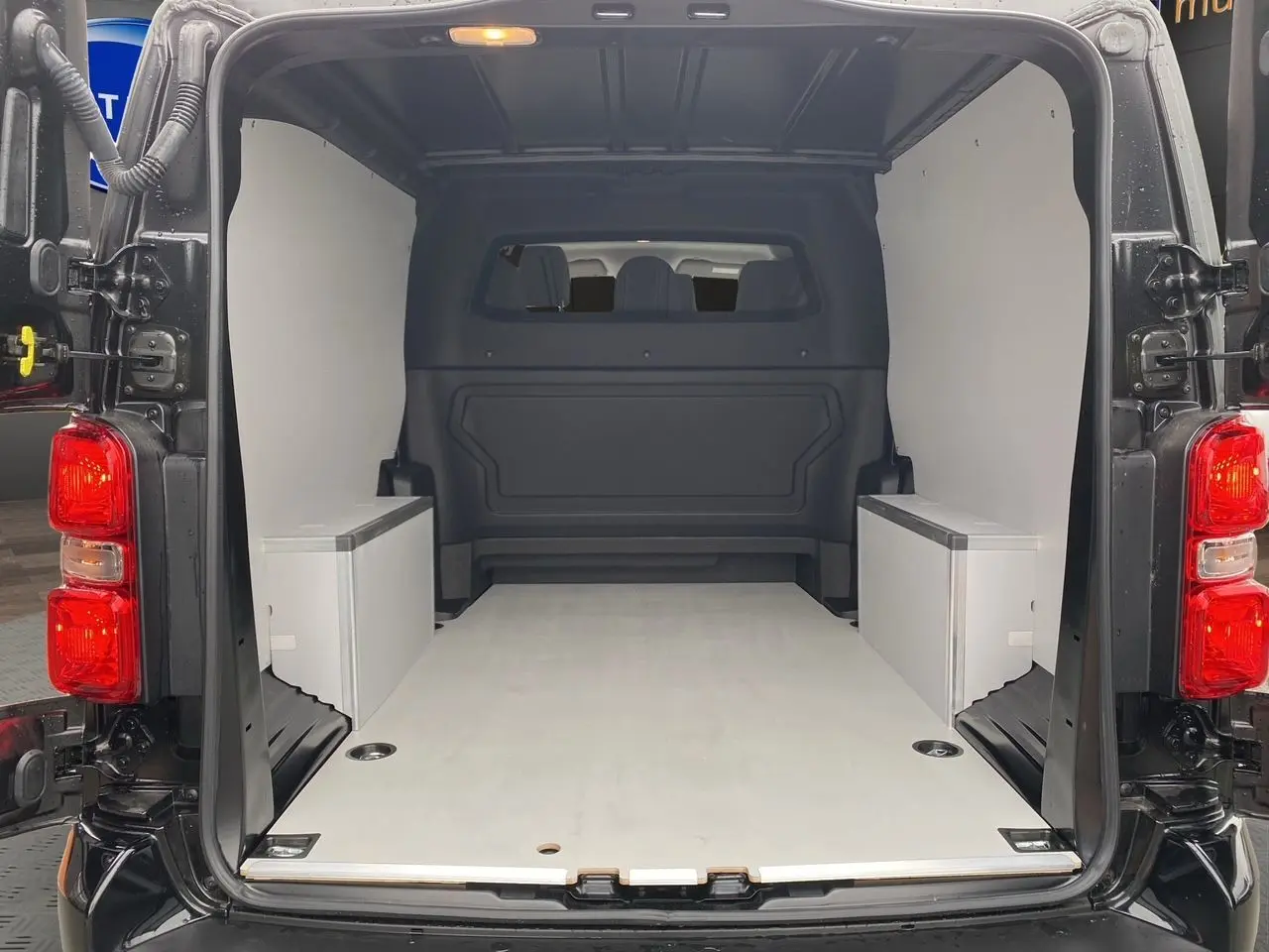 Vue arrière de l’intérieur noir et bois clair du fourgon Opel Vivaro 2025 avec plancher et habillage latéral en bois.
