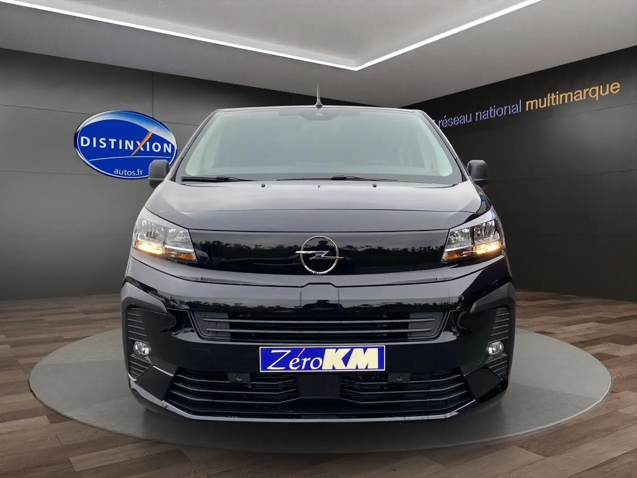 Vue frontale d'un Opel Vivaro noir 2025 avec feux allumés et plaque Zéro KM dans un showroom.