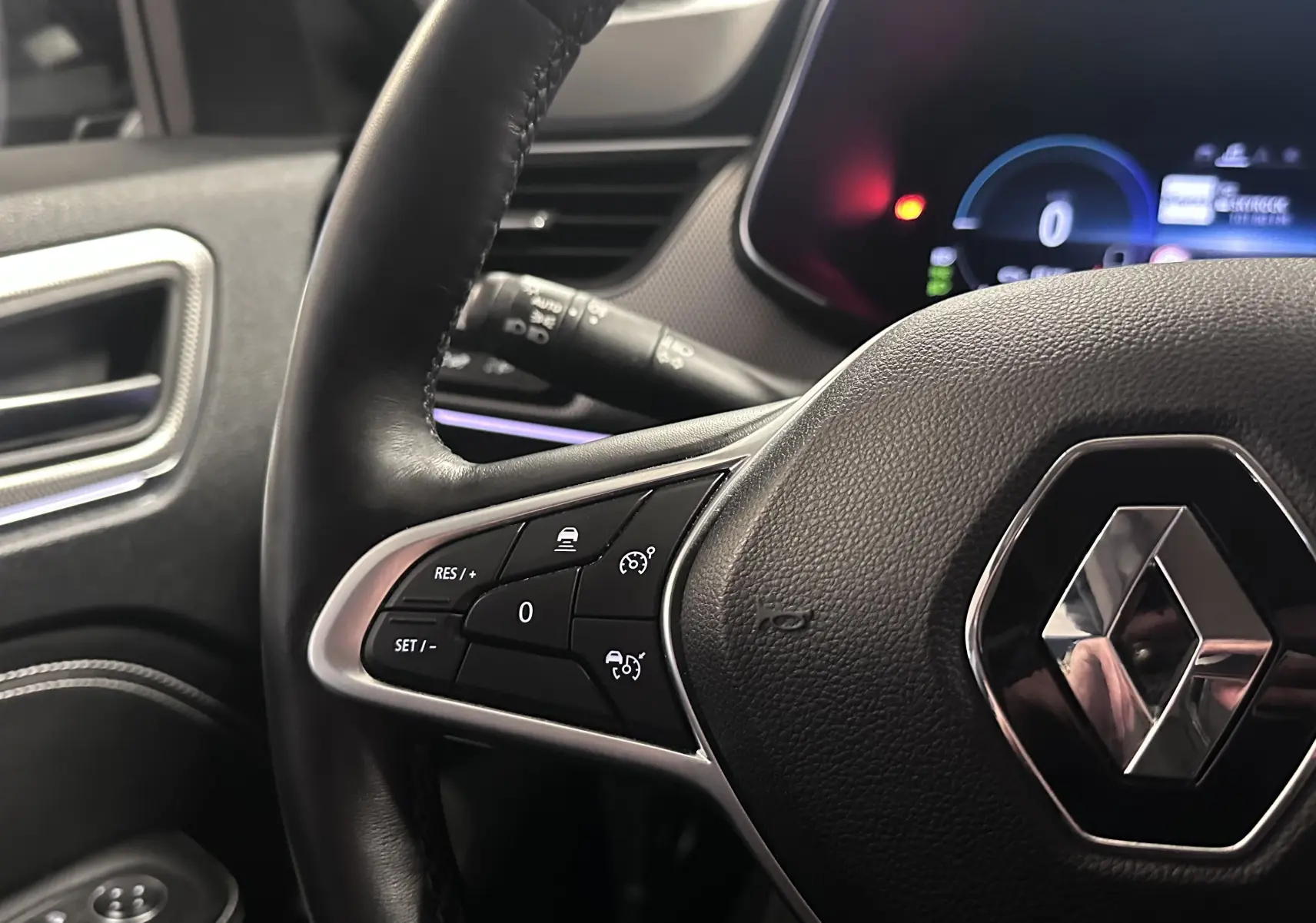 Gros plan sur le volant noir de la Renault Arkana 2022, avec commandes intégrées et tableau de bord numérique en arrière-plan.