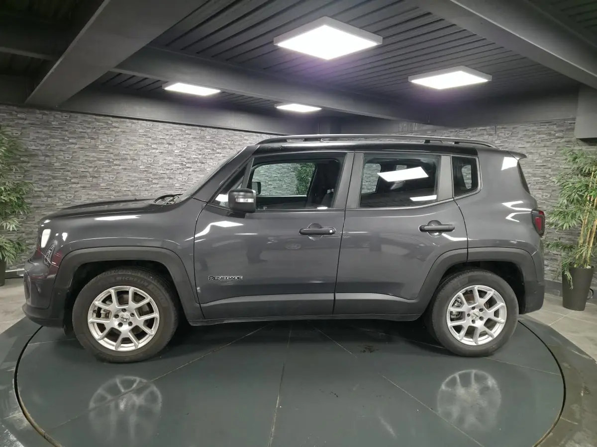 Jeep Renegade gris métallisé vu de profil côté gauche avec toit noir et jantes alliage 17 pouces en intérieur showroom.