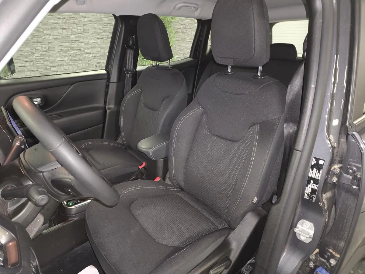 Vue intérieure côté conducteur du Jeep Renegade gris, sièges tissu noir avec accoudoir central et volant visible.