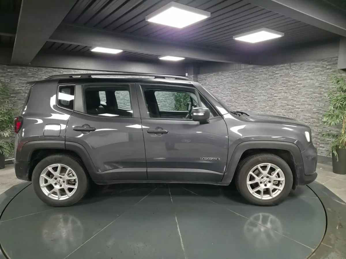 Profil côté gauche d'un Jeep Renegade gris métallisé avec toit noir et jantes alliage 17 pouces en intérieur showroom.