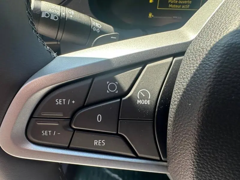 Gros plan sur les commandes multifonctions au volant du Dacia Duster 2026, boutons noirs avec marquages blancs.