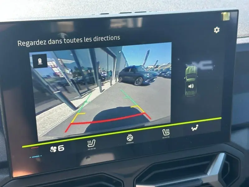 Écran tactile montrant la caméra de recul avec vue arrière d’un Dacia Duster Vert Cèdre métallisé stationné près d’un bâtiment.