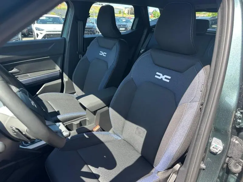Vue intérieure côté conducteur du Dacia Duster 2026 vert cèdre, sièges tissu Denim avec logo Dacia réfléchissant.