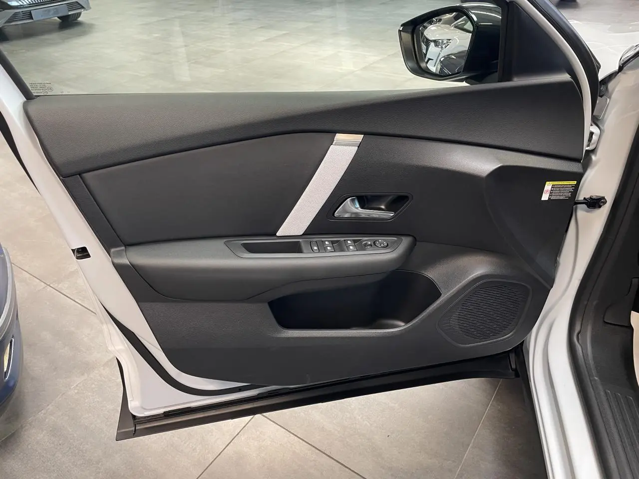 Vue intérieure de la porte avant gauche blanche d’une Citroën C4 2026 avec garniture noire et commande de vitres.