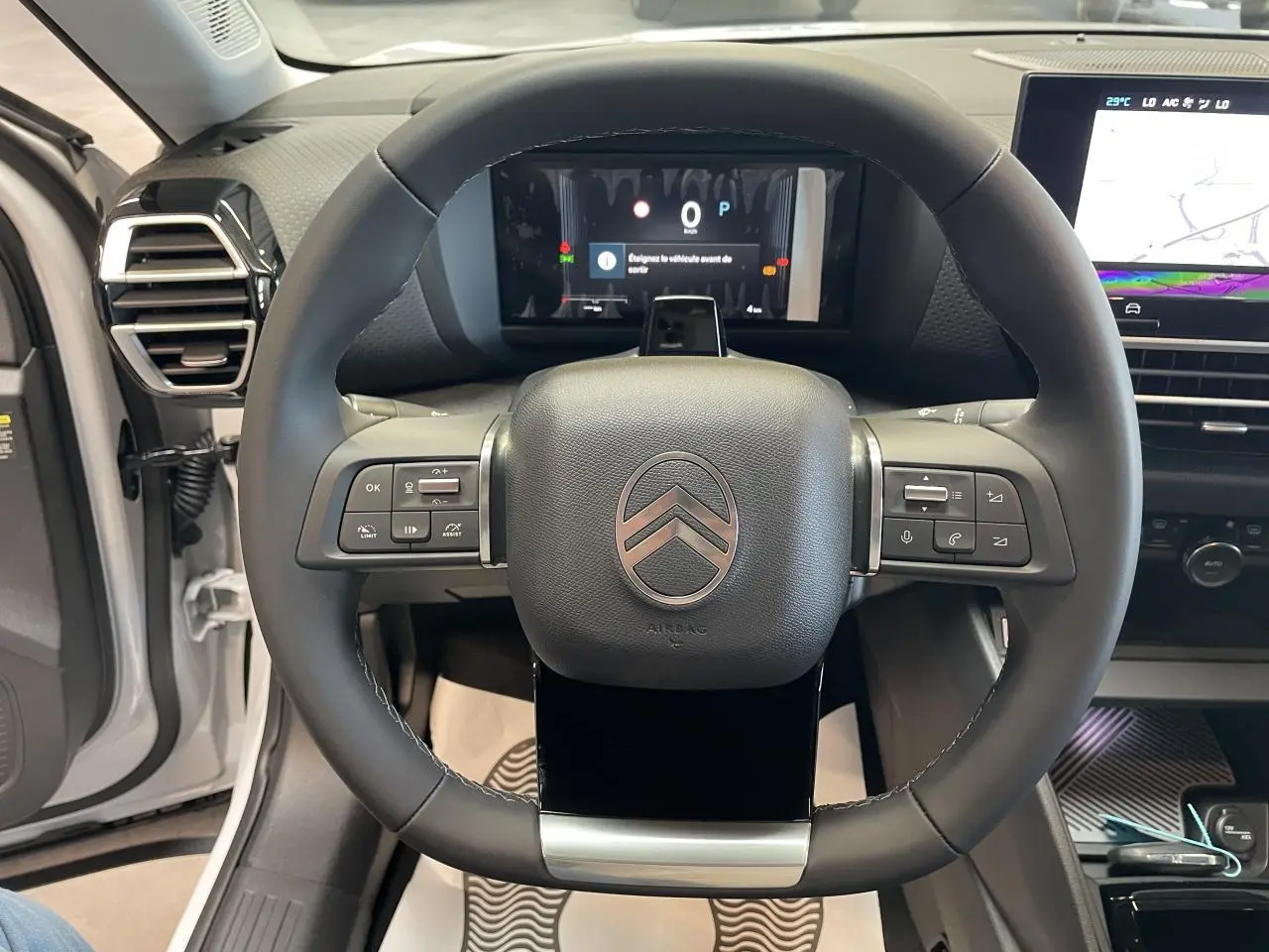 Vue rapprochée du volant cuir noir et du tableau de bord numérique d'une Citroën C4 blanche, intérieur moderne.