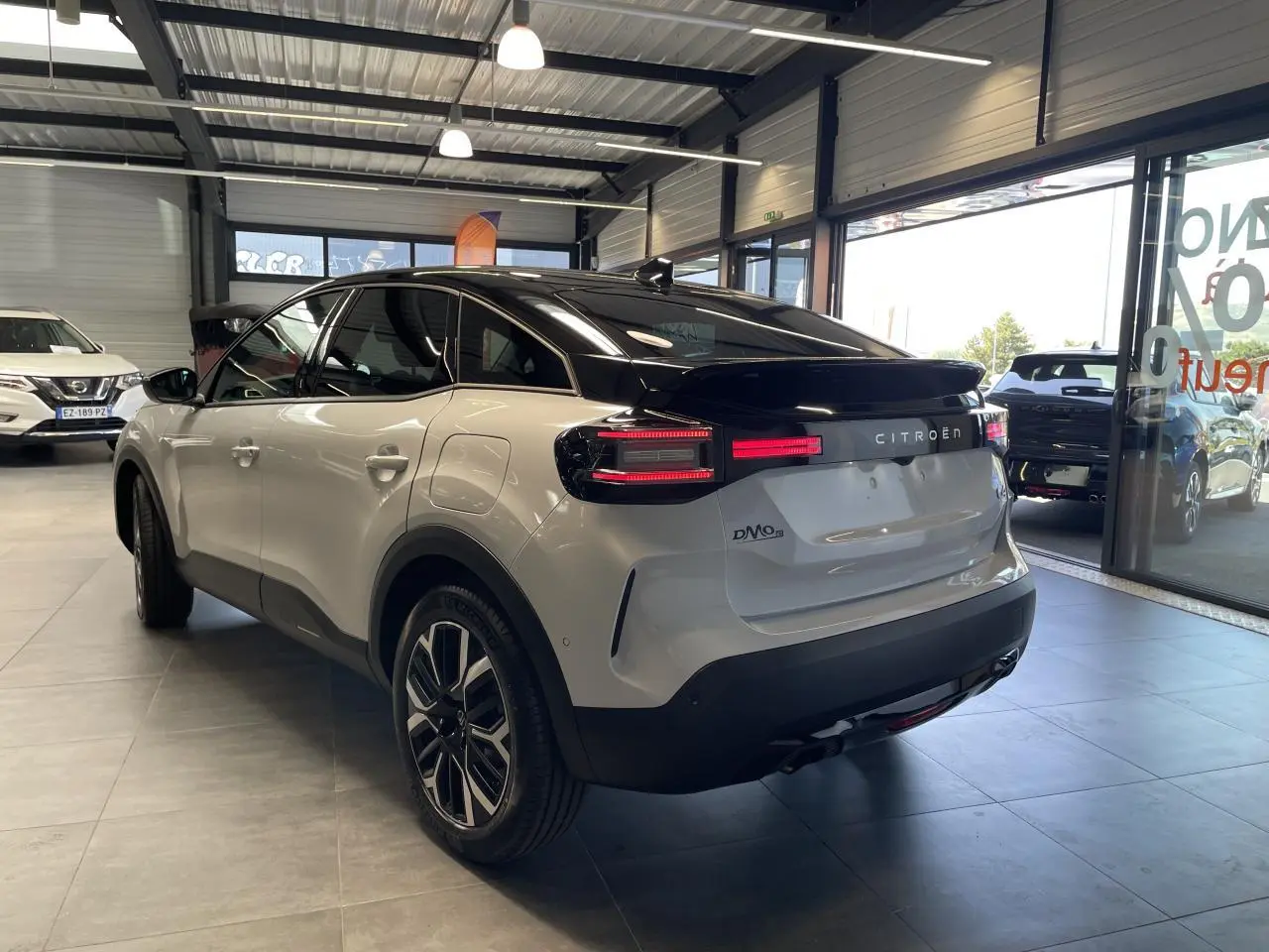 Vue 3/4 arrière droite d'une Citroën C4 blanche avec toit noir et jantes alliage 18 pouces dans un showroom.