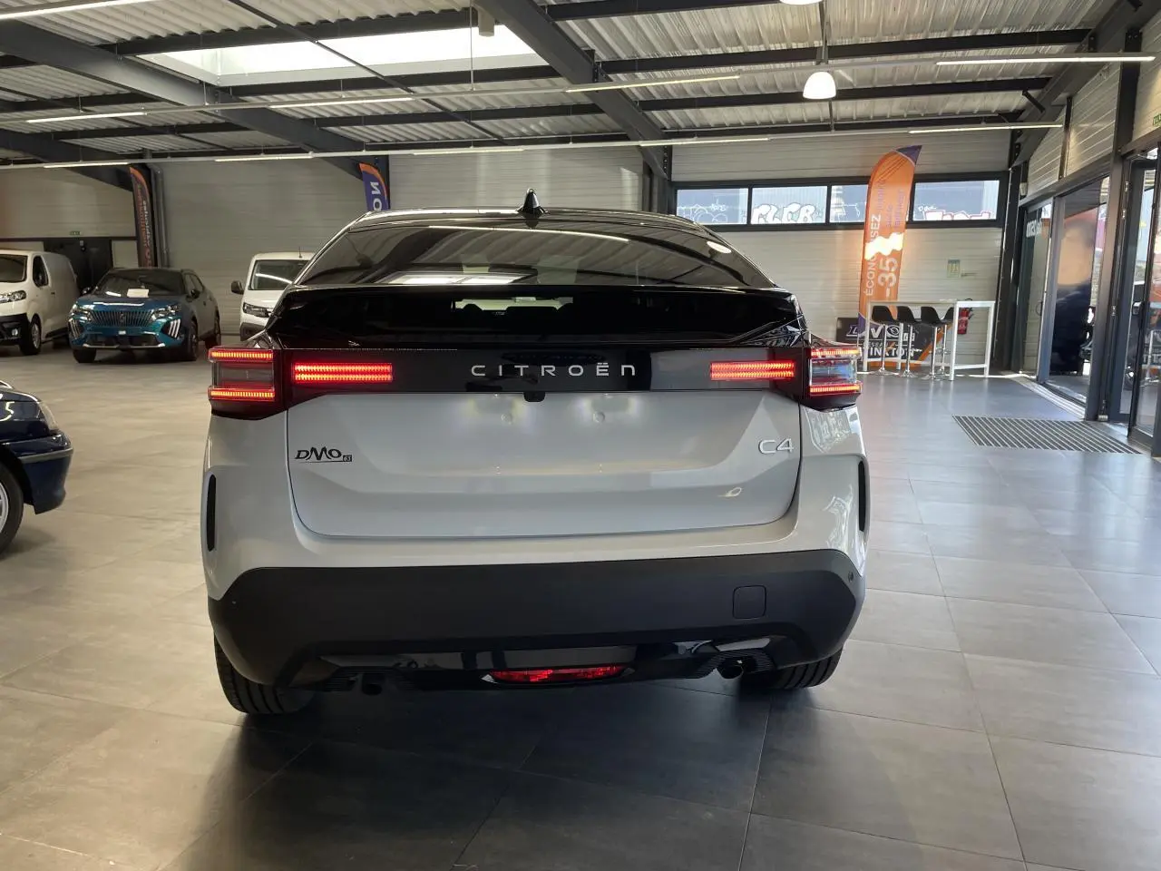 Vue arrière d'une Citroën C4 blanche avec toit noir Perla Nera et feux arrière LED allumés en intérieur showroom.