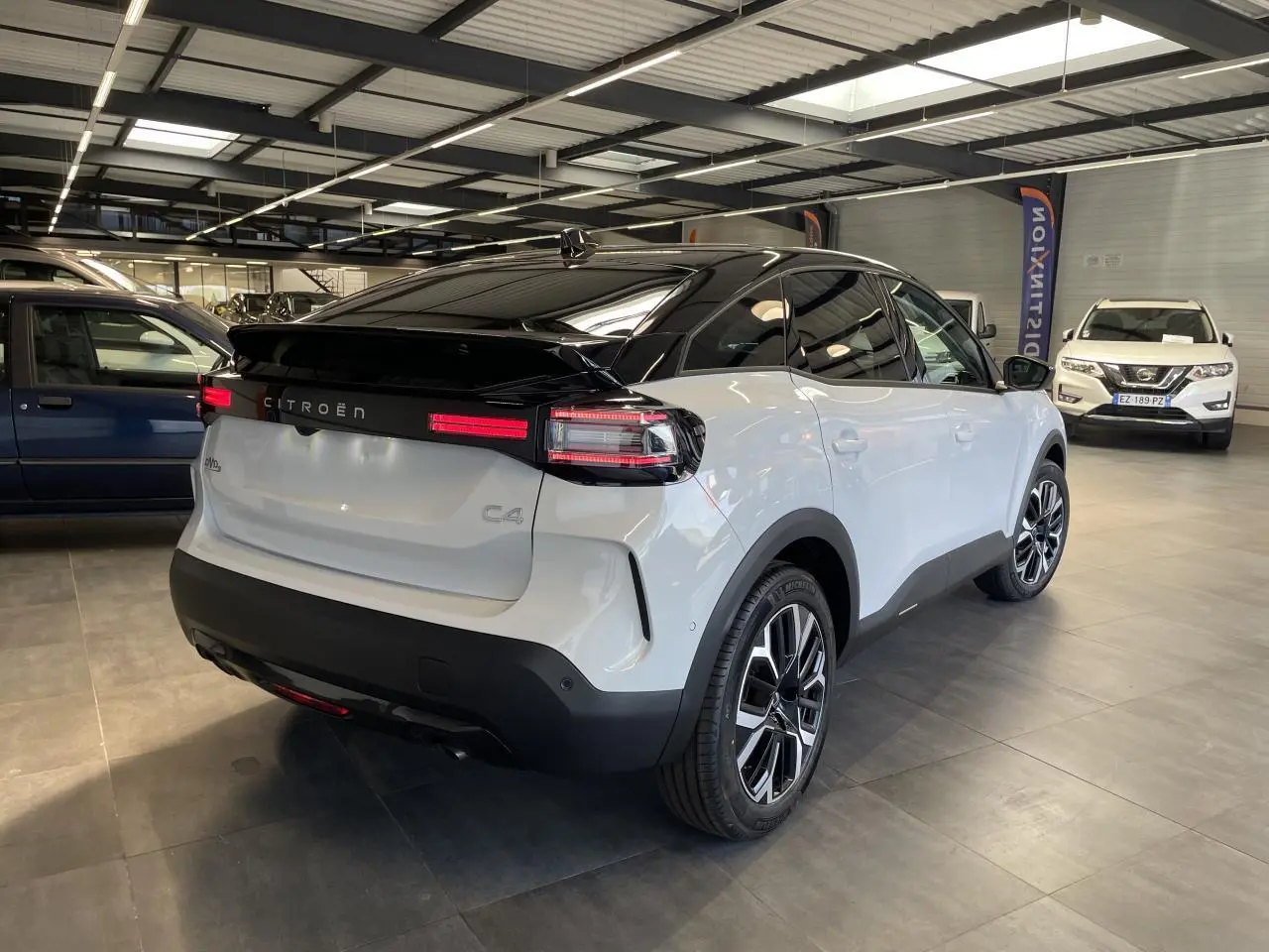Vue 3/4 arrière droite d'une Citroën C4 blanche avec toit noir et jantes alliage 18 pouces en showroom.