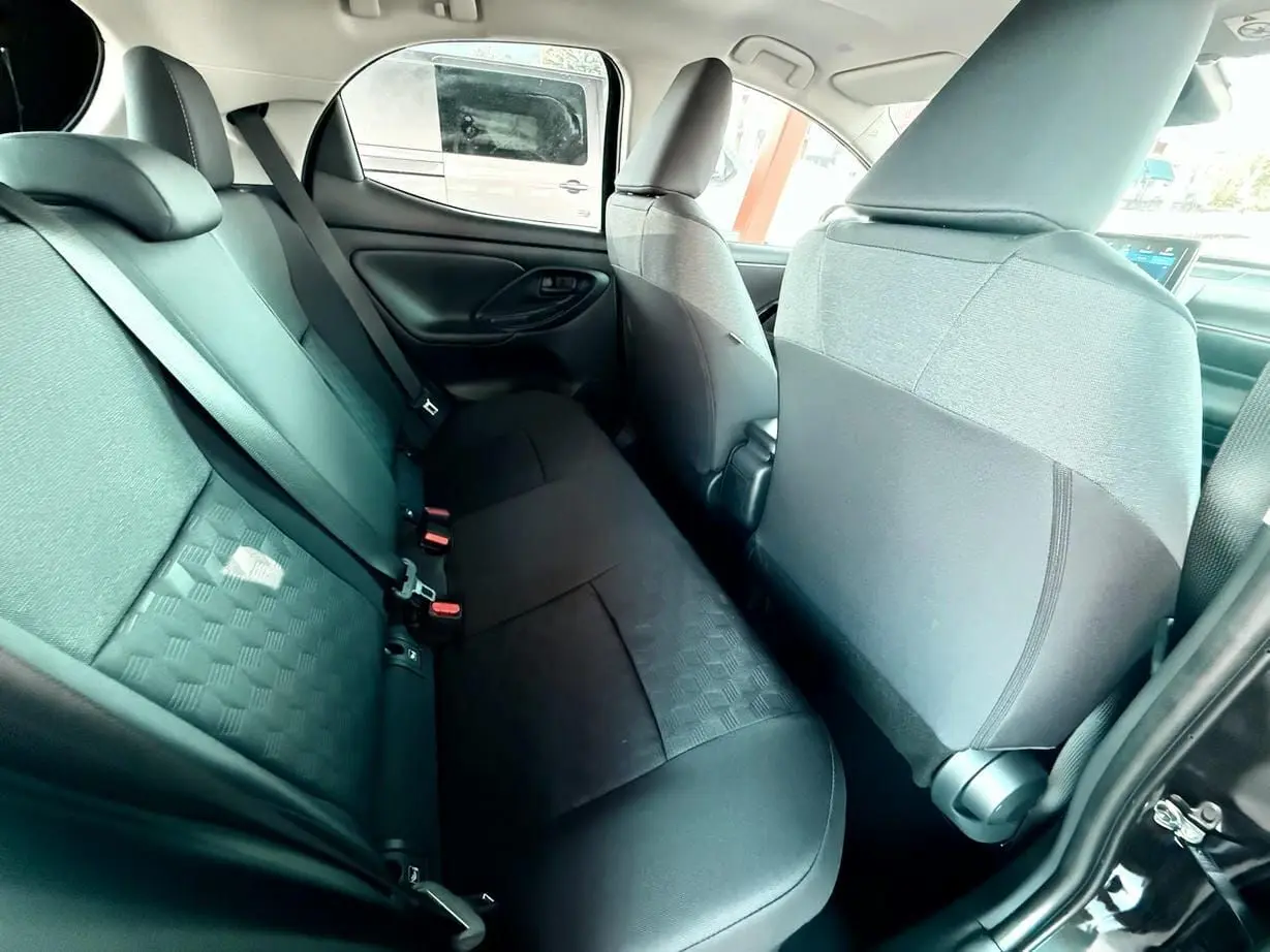 Intérieur arrière de la Toyota Yaris Hybrid 2025, sièges noirs en tissu avec motifs géométriques, vue côté gauche.