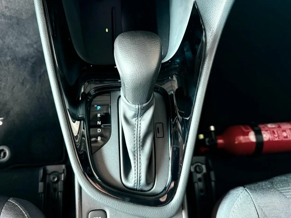 Le levier de vitesse automatique noir de la Toyota Yaris Hybrid 2025 vu de dessus avec un extincteur rouge à côté.
