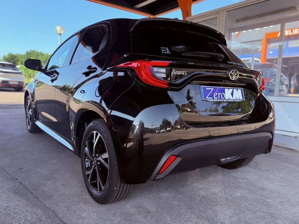 Vue 3/4 arrière droite d'une Toyota Yaris hybride noire 2025 avec feux arrière LED et jantes noires.