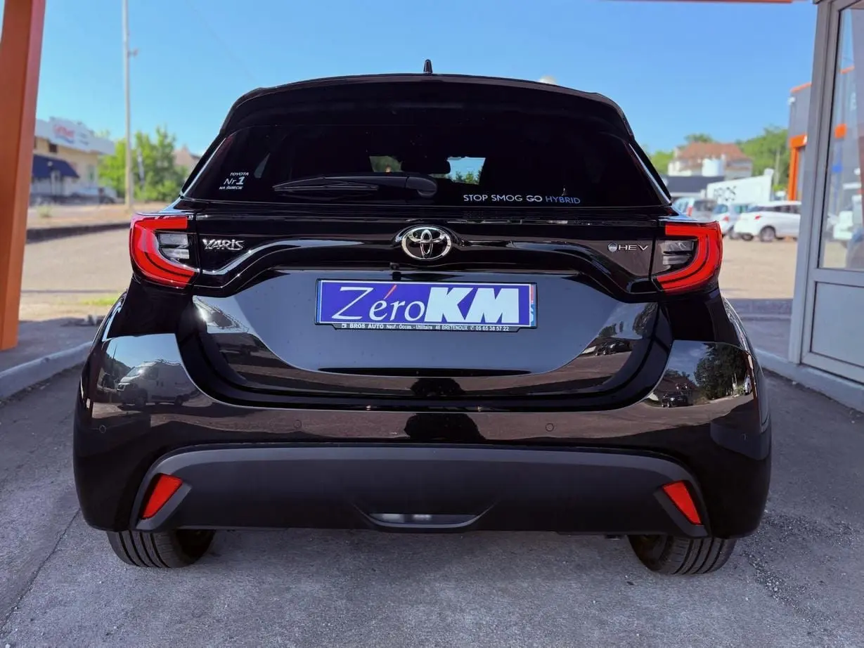 Vue arrière d'une Toyota Yaris Hybrid noire avec feux arrière LED et logo HEV sur un parking extérieur.