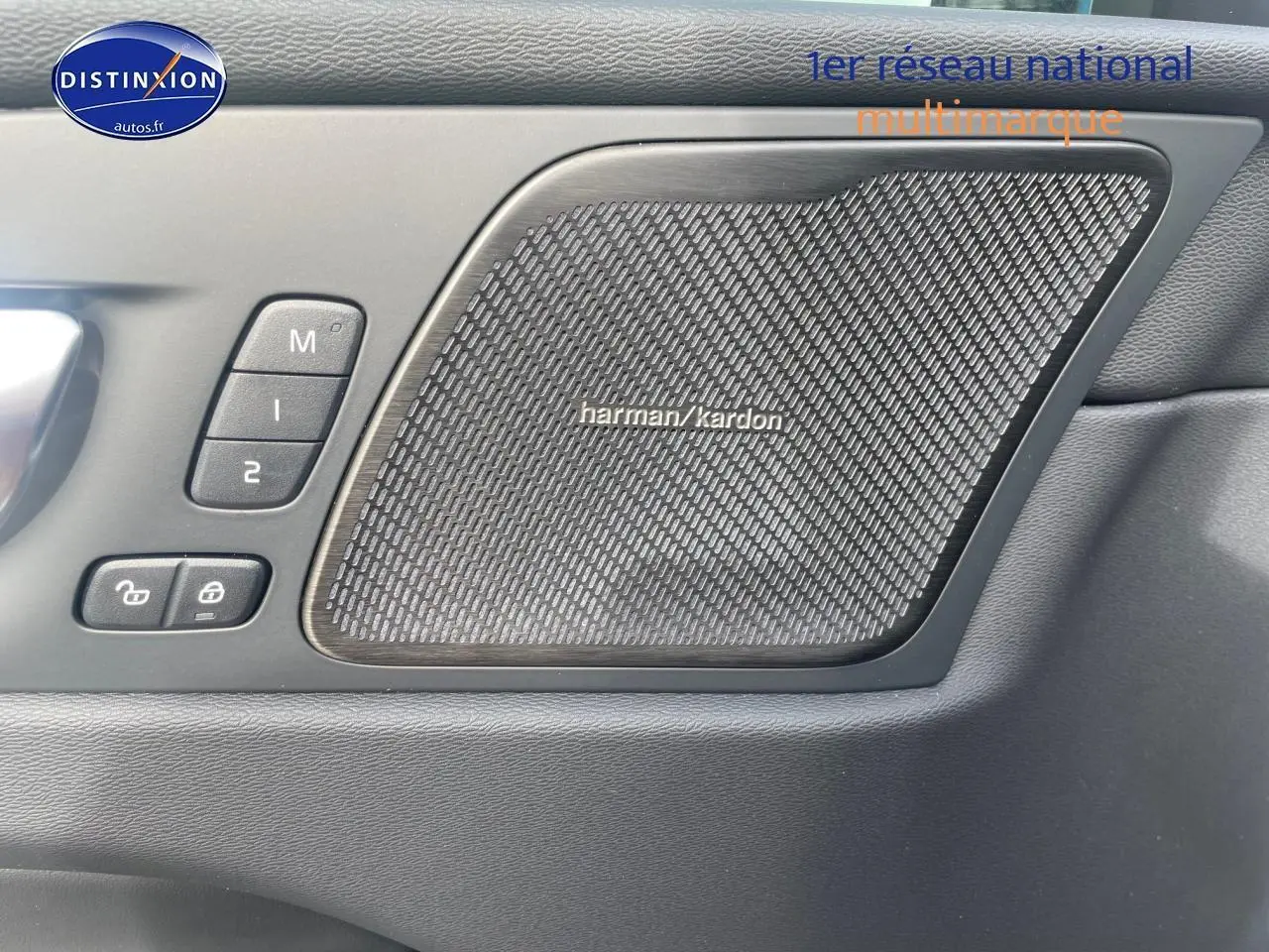 Gros plan sur la porte avant gauche du Volvo XC60 gris, mettant en valeur l'enceinte Harman Kardon et les commandes mémoire sièges.