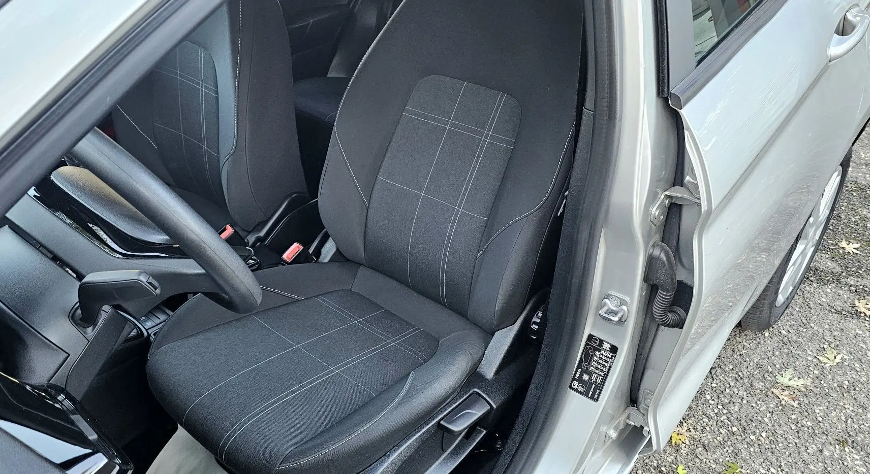 Vue intérieure côté conducteur de la Ford Fiesta gris lunaire, mettant en valeur le siège tissu noir à motifs gris et le volant.