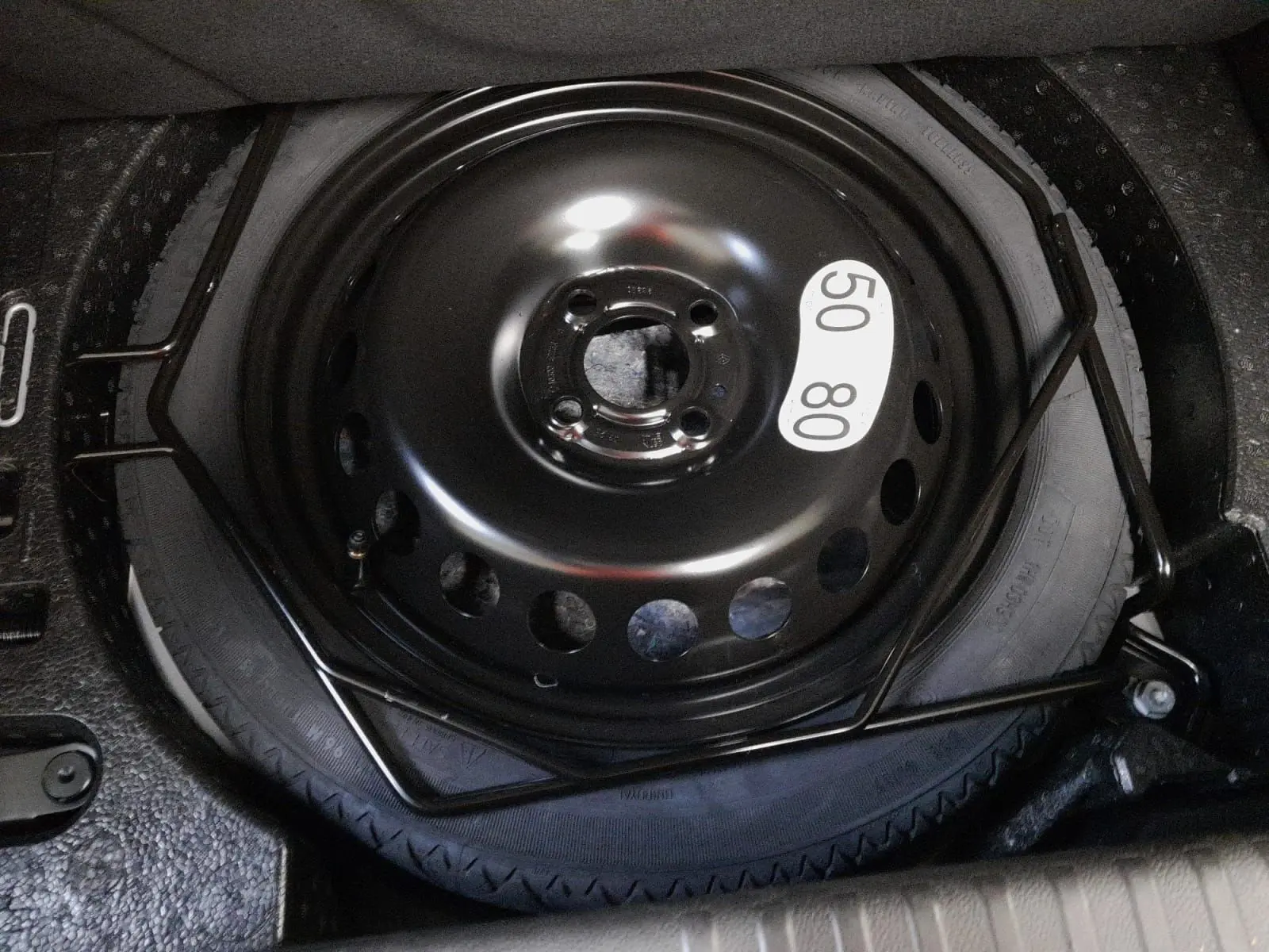 Gros plan sur la roue de secours temporaire noire dans le coffre de la Renault Clio V gris schiste 2025.