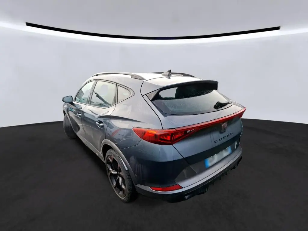 Vue 3/4 arrière droite d'un CUPRA Formentor gris avec feux arrière en bandeau lumineux et jantes noires 19 pouces.