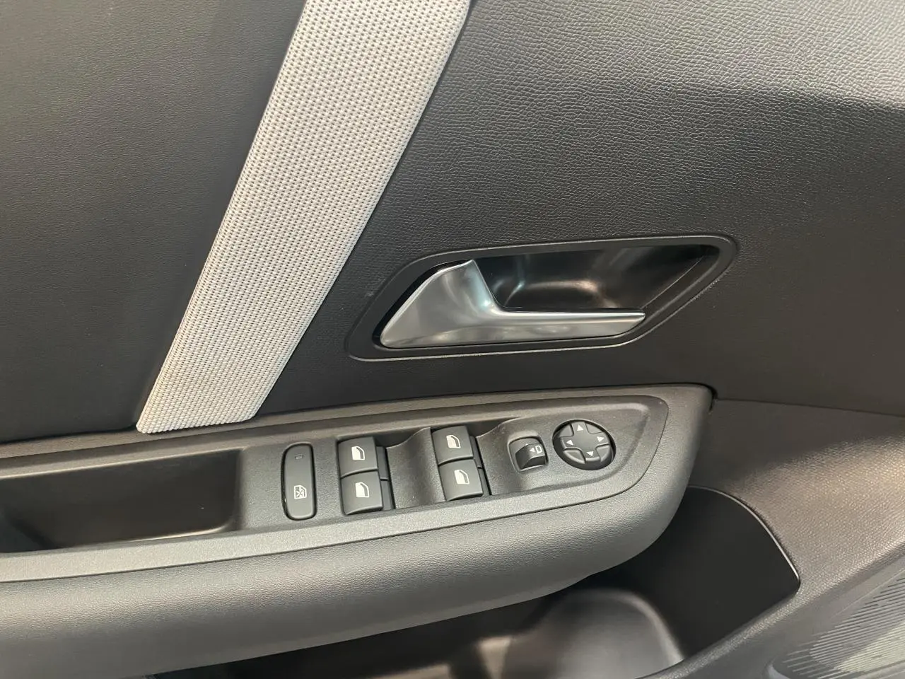 Gros plan sur la porte côté gauche de la Citroën C4 gris, montrant la poignée intérieure et les commandes des vitres électriques.