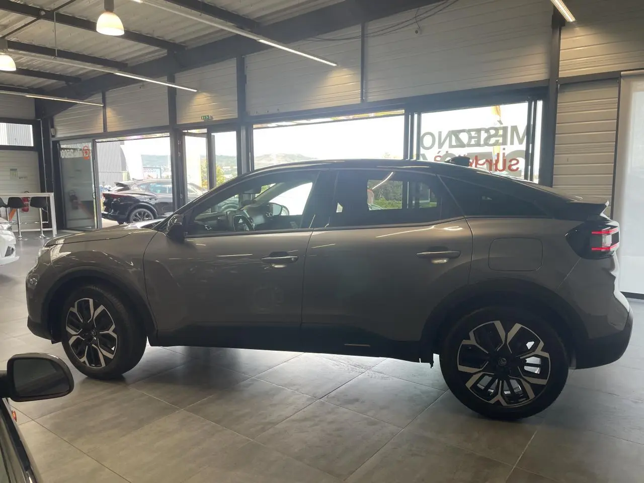 Vue de profil côté gauche d'une Citroën C4 gris métallisé avec jantes alliage 18'' et toit bi-ton noir en showroom.