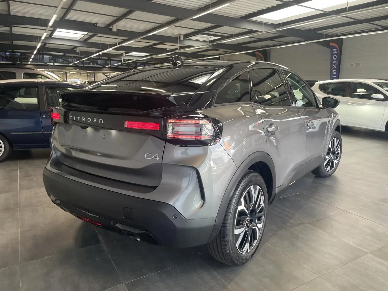 Vue 3/4 arrière droite d'une Citroën C4 gris métallisé avec toit noir et feux arrière LED en intérieur showroom.