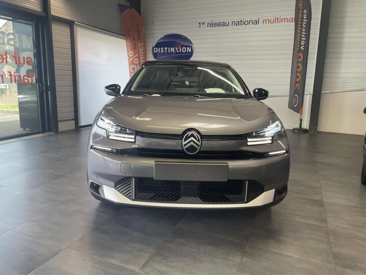 Vue avant d'une Citroën C4 gris métallisé avec toit noir dans un showroom, mettant en valeur ses phares LED distinctifs.