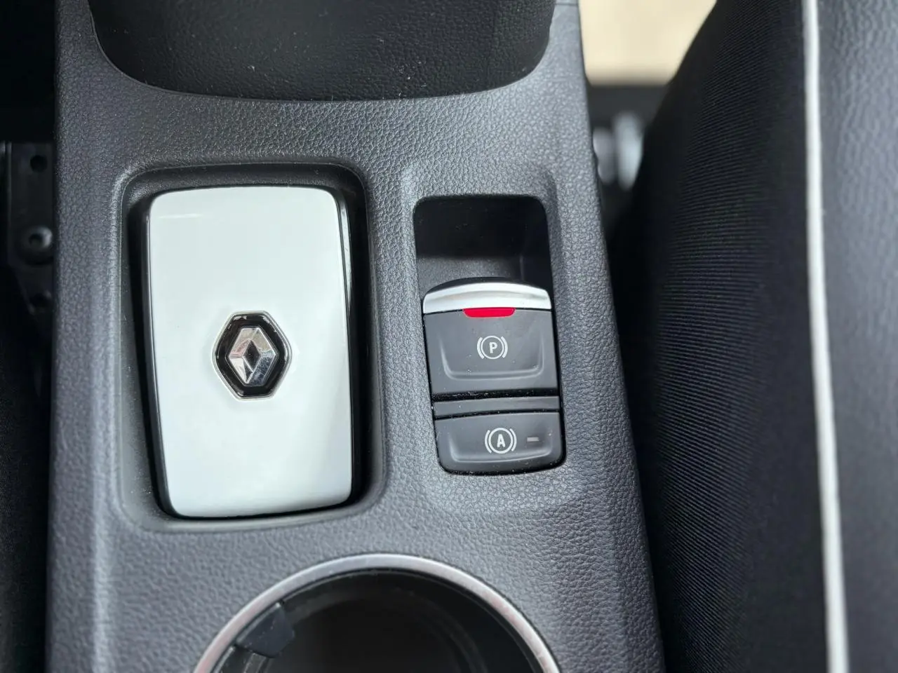 Gros plan sur la console centrale noire du Renault Captur 2024 avec bouton frein de parking électrique et logo Renault blanc.