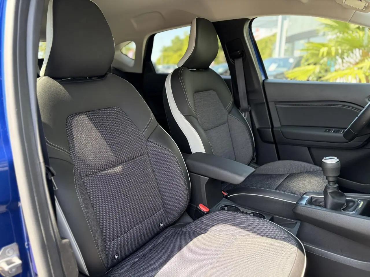 Vue intérieure côté conducteur du Renault Captur 2024, sièges bi-matière gris et noir avec accoudoir central.