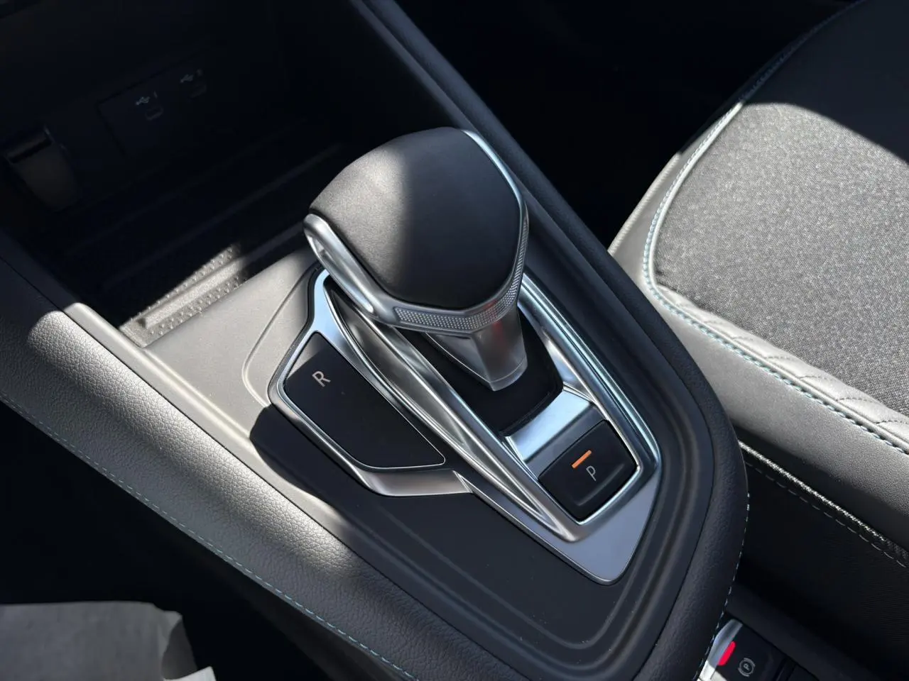 Le levier de vitesse automatique noir et chrome de la Renault SYMBIOZ 1.6 E-Tech, avec surpiqûres bleues sur la console.