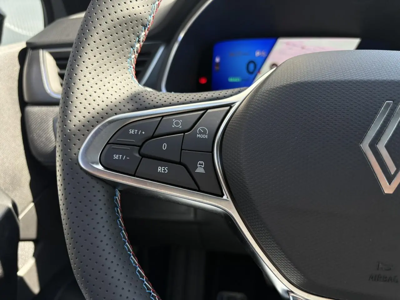 Gros plan sur le volant perforé avec surpiqûres bleu blanc rouge du Renault Symbioz 2025, boutons de commande visibles.