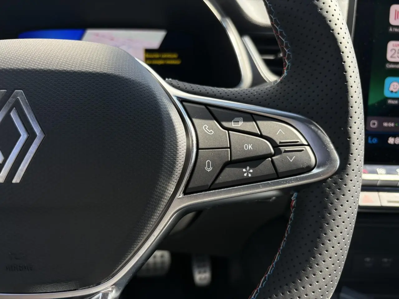 Gros plan sur le volant perforé du Renault Symbioz gris Rafale, avec commandes intégrées et surpiqûres tricolores.