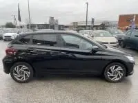 Vue de profil côté gauche d'une Hyundai i20 2025 noir Phantom Metal avec jantes alliage et vitres teintées, sur parking urbain.