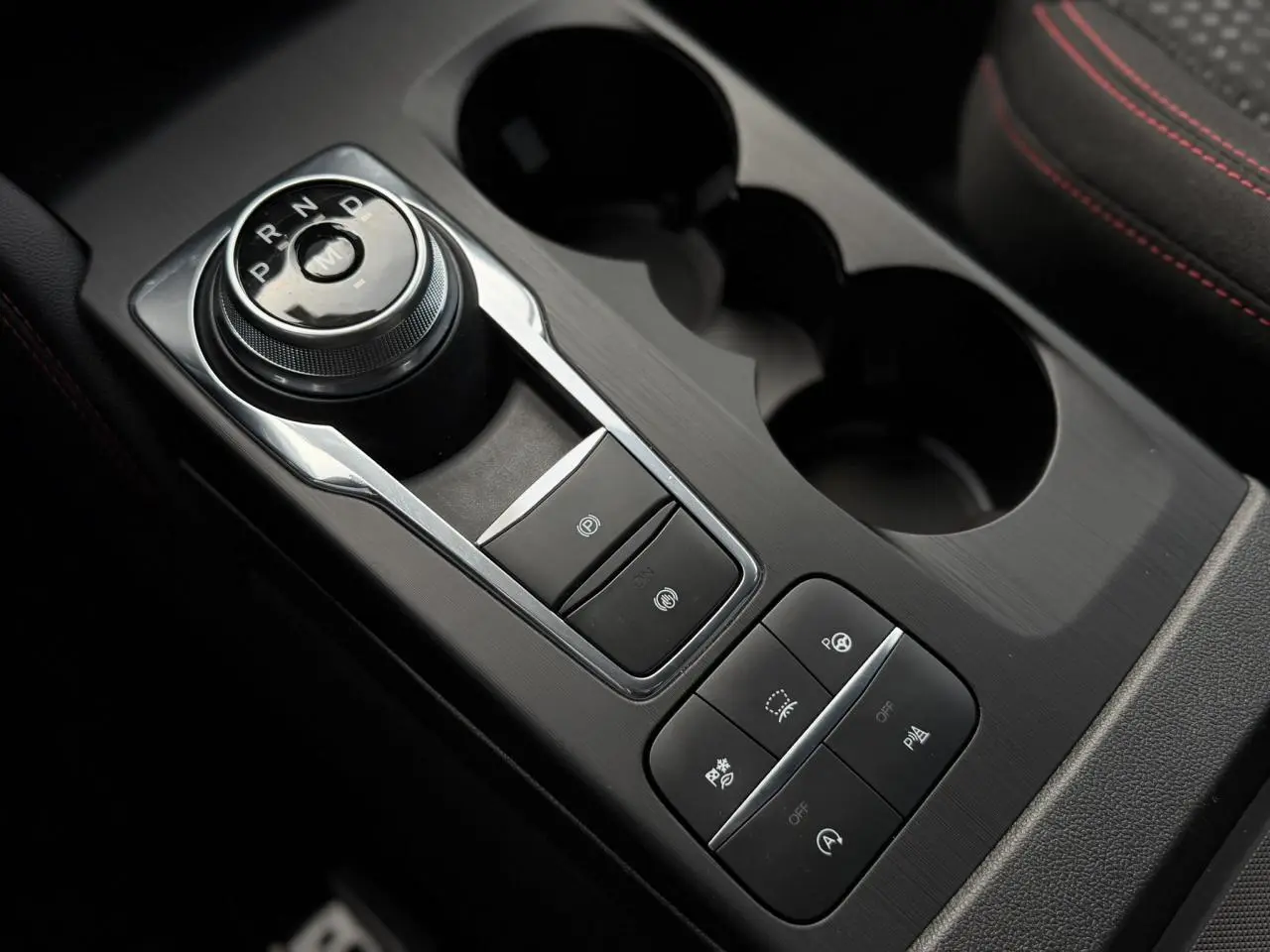 Gros plan sur la console centrale noire du Ford Kuga 2023 avec sélecteur rotatif de boîte auto et boutons de contrôle.