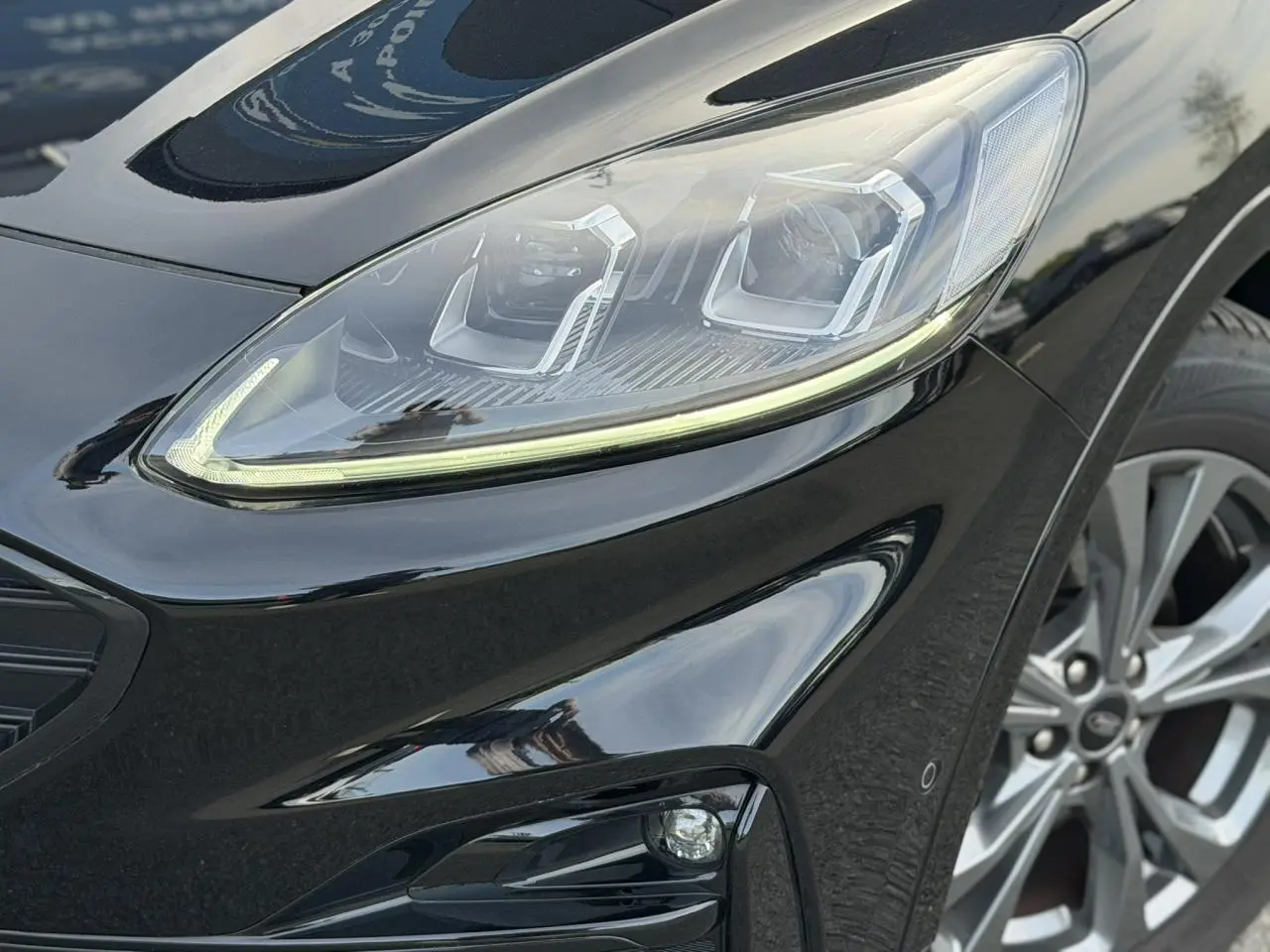 Gros plan sur le phare avant droit et la roue alliage 18 pouces du Ford Kuga noir Agathe finition ST-Line.