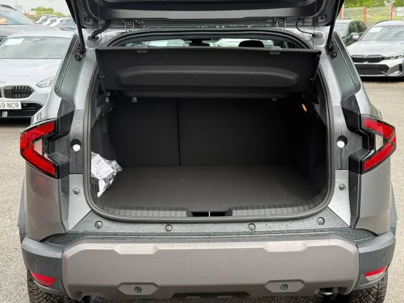 Vue arrière du coffre ouvert d'un Dacia Duster gris schiste 2026, avec hayon relevé et feux arrière visibles.