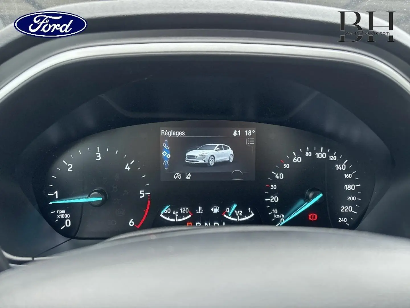 Vue rapprochée du tableau de bord de la Ford Focus 2020, affichage numérique avec indicateurs bleus et image véhicule blanche.
