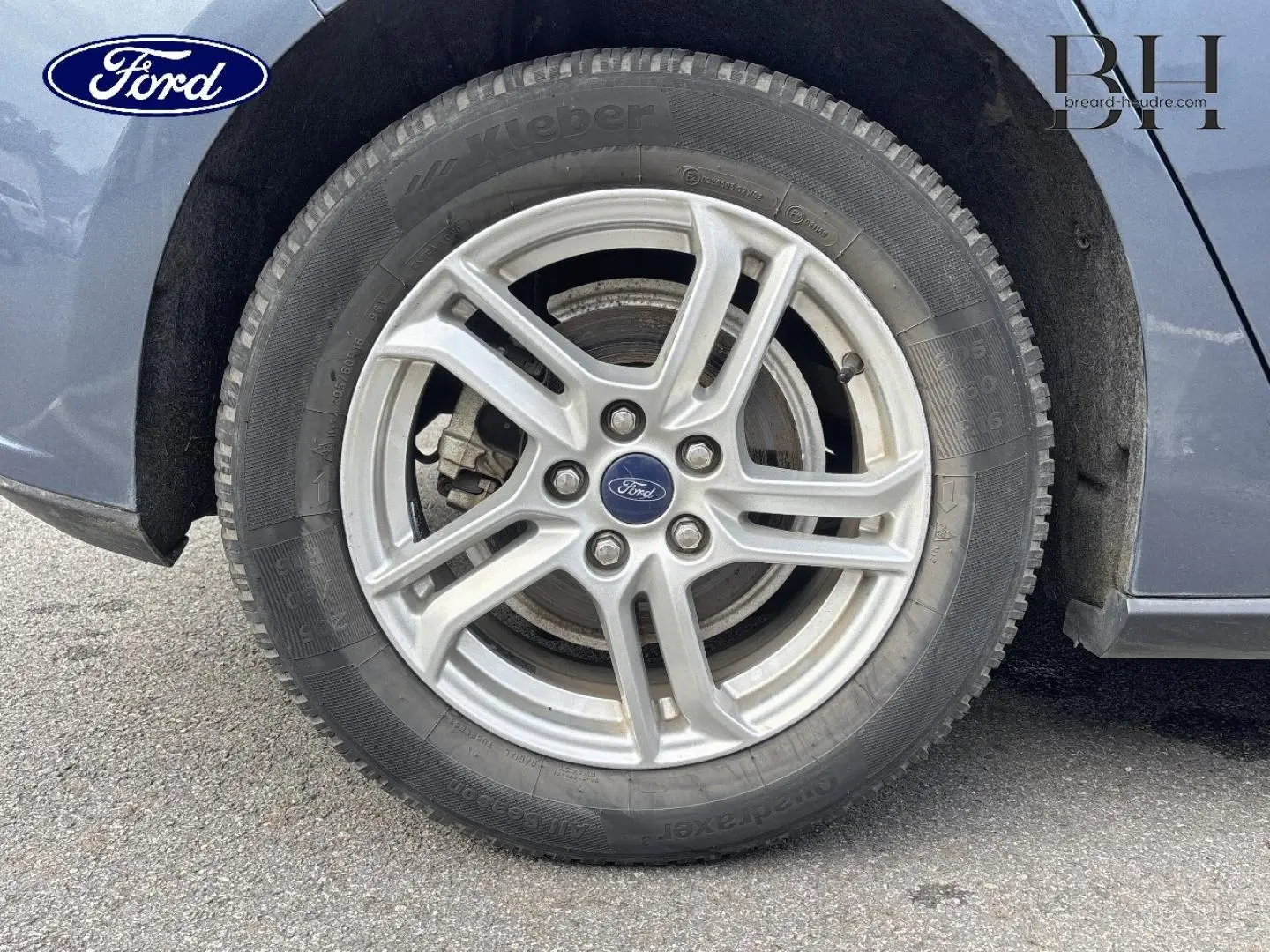 Gros plan sur la roue avant droite avec jante alu argentée d'une Ford Focus bleu azur métallisé.