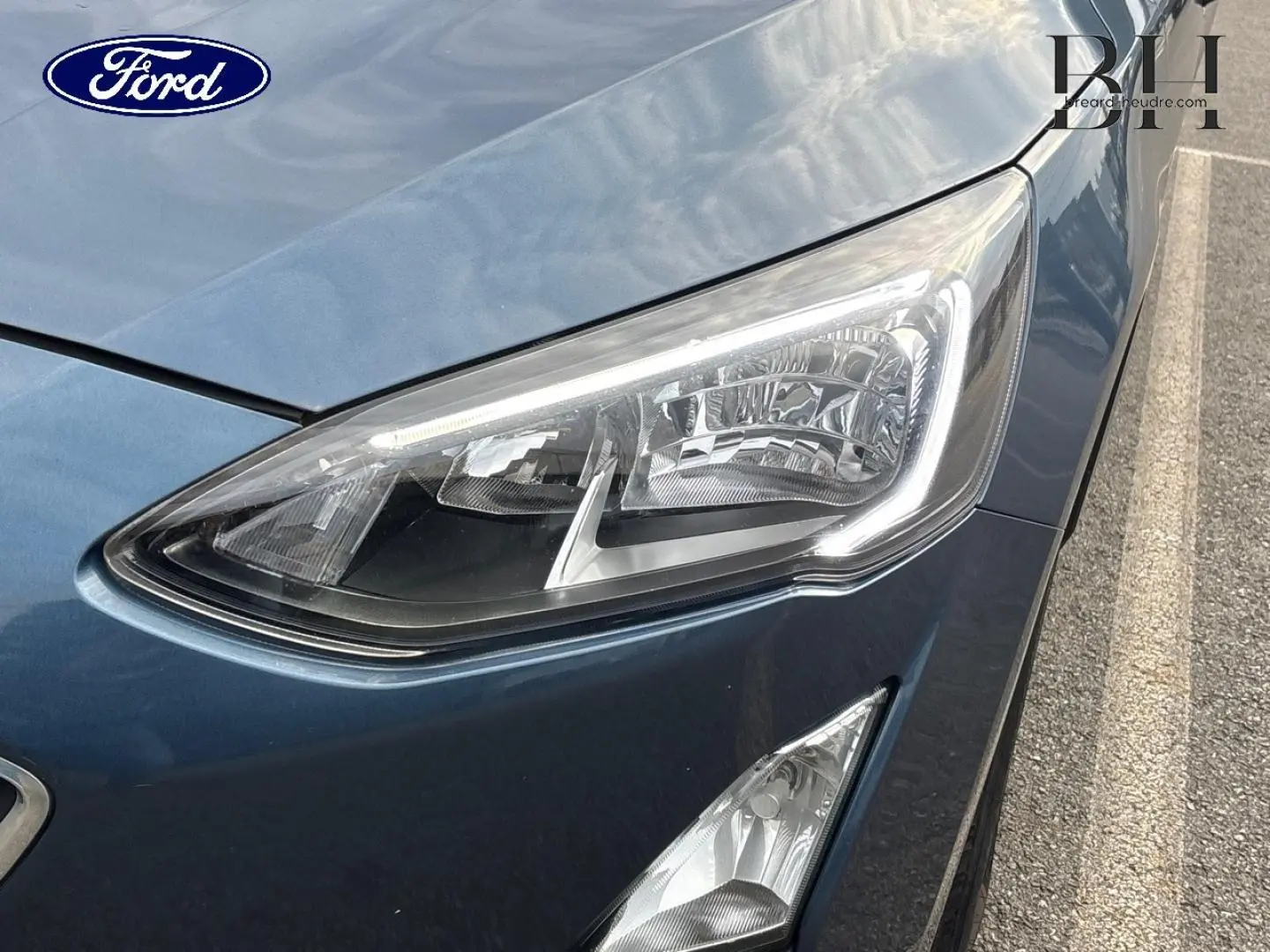 Gros plan sur le phare avant droit d’une Ford Focus 1.5 EcoBlue bleu azur métallisé avec détails du capot et pare-chocs.