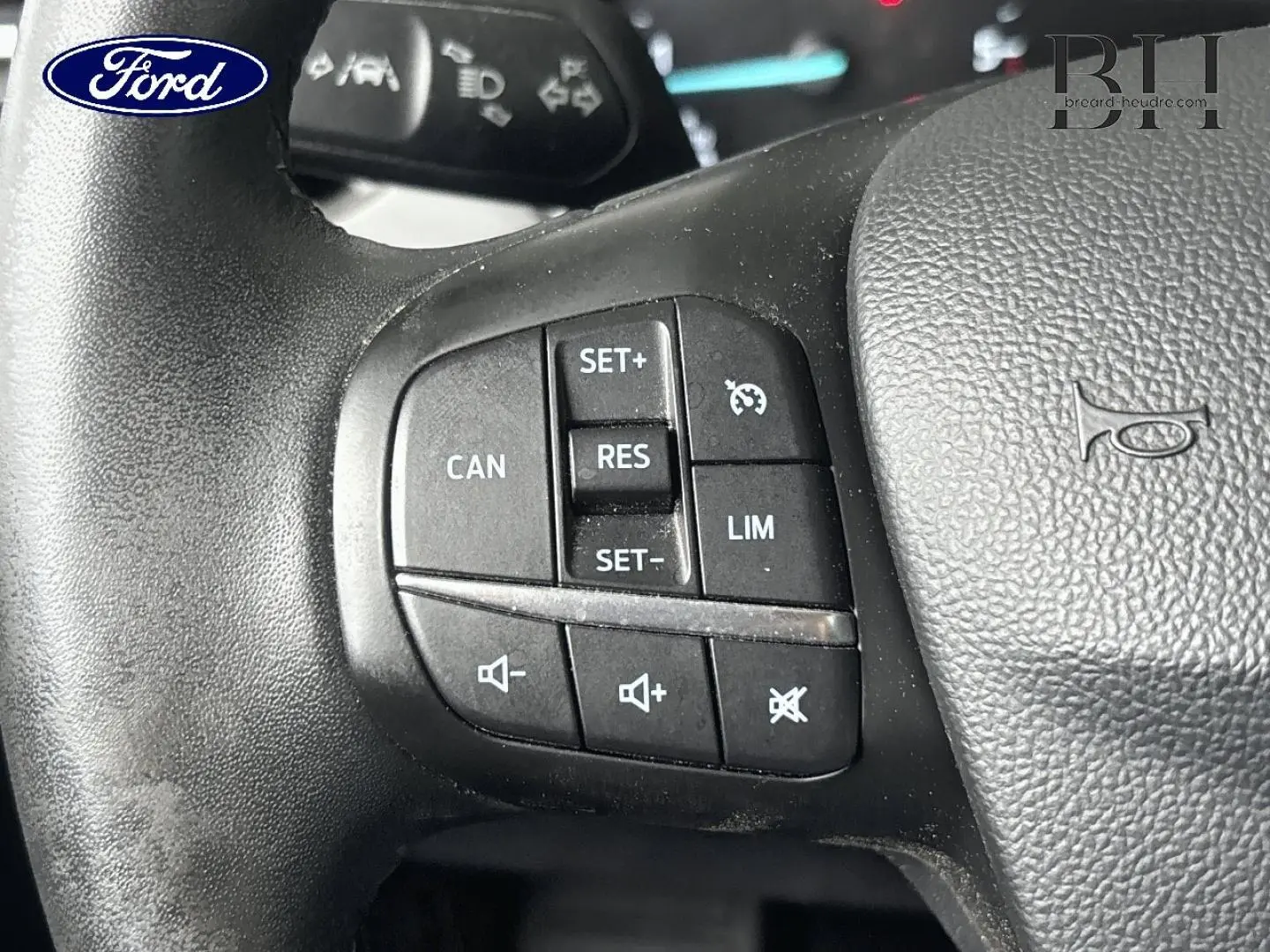 Gros plan sur les commandes du volant cuir noir d'une Ford Focus bleu azur métallisé, boutons multifonctions visibles.