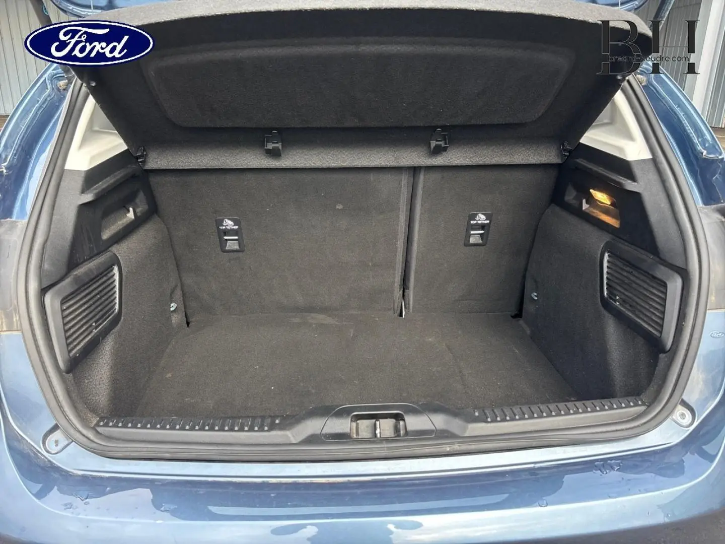 Coffre ouvert vu de l'arrière d'une Ford Focus bleu azur métallisé, montrant l'espace de chargement vide.