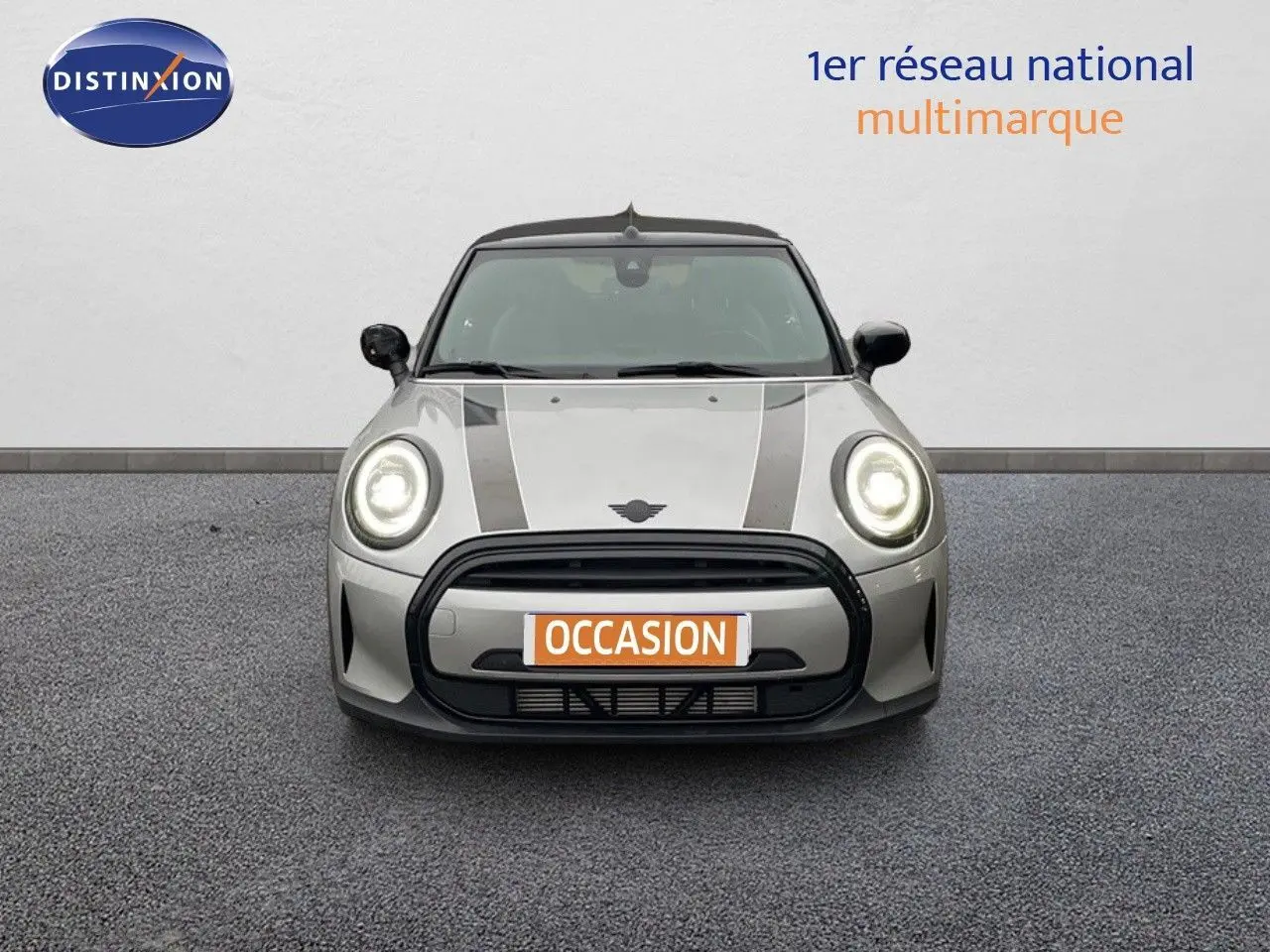 Vue frontale d'une MINI Cabriolet 2023 couleur Melting Silver Metal avec phares allumés et bandes noires sur le capot.